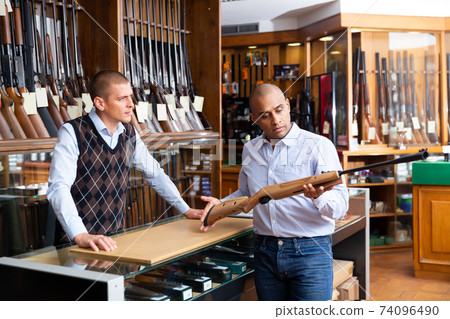 Hispanic man examining hunting rifle and consulting with salesman 74096490