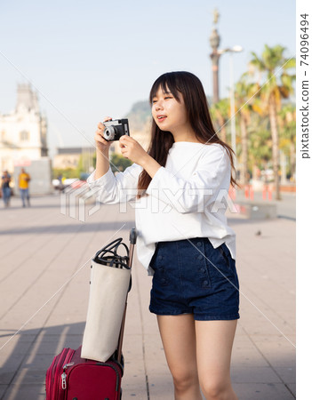 Smiling young girl holding camera in hands and photographing in city Smiling young girl holding camera in hands and photographing in city 74096494