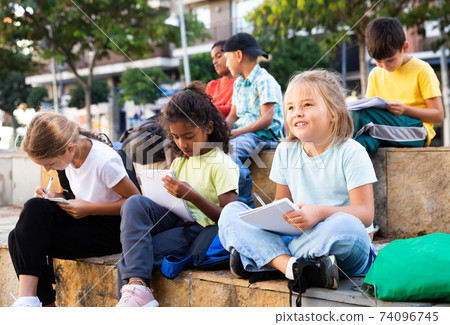 Schoolchildren sitting with workbooks in schoolyard in autumn day Schoolchildren sitting with workbooks in schoolyard in autumn day 74096745