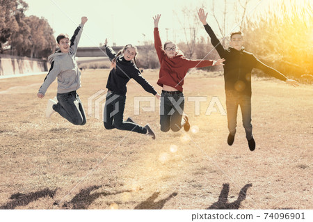 Friendly teenagers jumping together in park 74096901