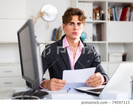Upset attractive young businessman working documents and laptop Upset attractive young businessman working documents and laptop 74097115