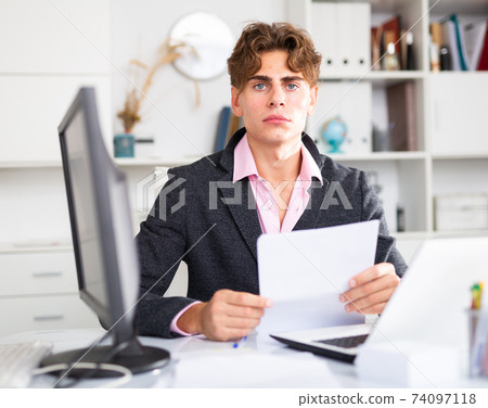 Upset attractive young businessman working documents and laptop Upset attractive young businessman working documents and laptop 74097118