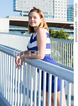 Girl in blue dress standing on city bridge Girl in blue dress standing on city bridge 74097120