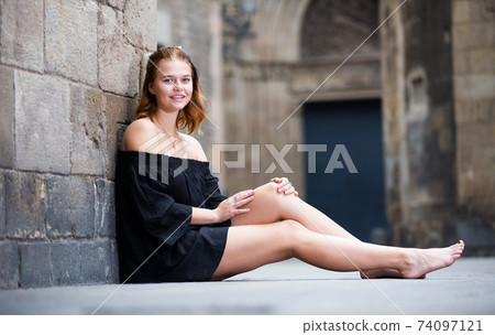 Positive girl sitting barefoot near the stone wall Positive girl sitting barefoot near the stone wall 74097121