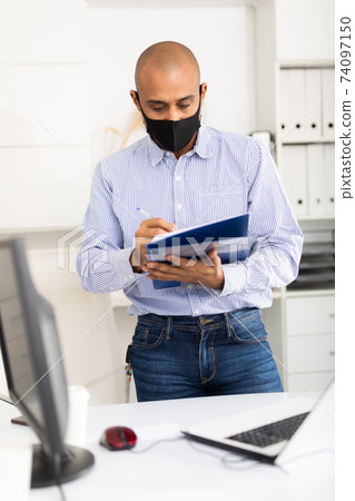 Businessman in protective mask makes notes in document 74097150