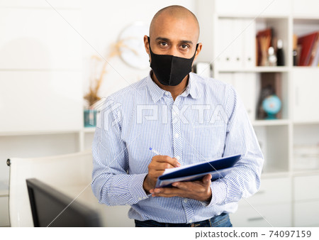 Portrait of positive business man in protective mask with folder of documents 74097159