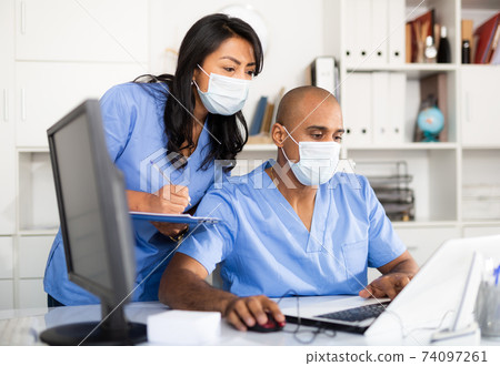Doctor and nurse in protective medical mask check patient data in hospital computer 74097261