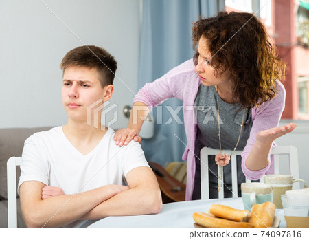 Frowning teenager listening to reprimanding from mother 74097816