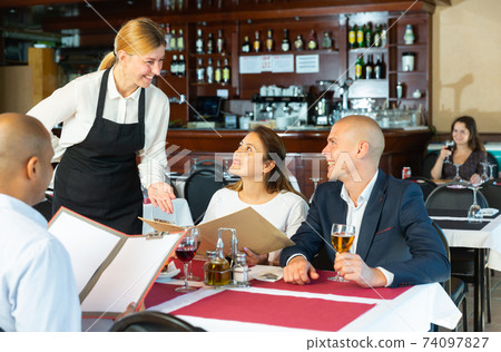 Restaurant guests will choose dish from the menu. Polite waitress helps with choice Restaurant guests will choose dish from the menu. Polite waitress helps with choice 74097827