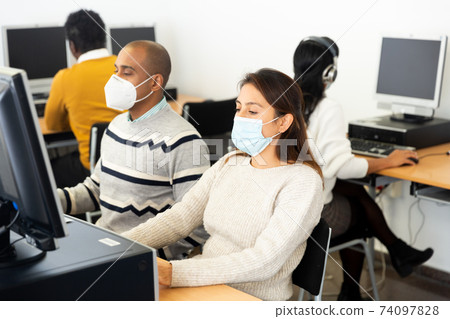 Female student in face mask working on computer in library Female student in face mask working on computer in library 74097828