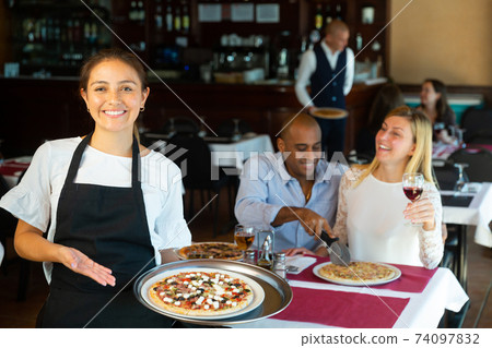 Hospitable latin american waitress meeting guests in pizzeria Hospitable latin american waitress meeting guests in pizzeria 74097832
