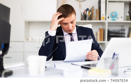 Pensive businessman working with papers Pensive businessman working with papers 74097834