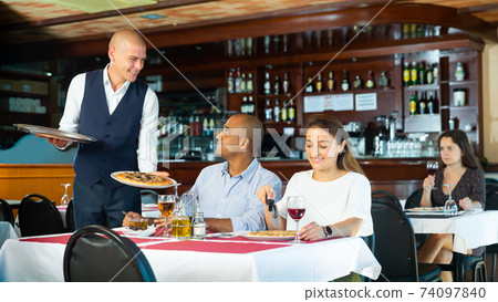Polite waiter bringing ordered pizza to couple visited restaurant for lunch 74097840