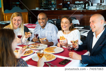 Happy friends eating delicious pizza and chatting with each other in restaurant Happy friends eating delicious pizza and chatting with each other in restaurant 74097863