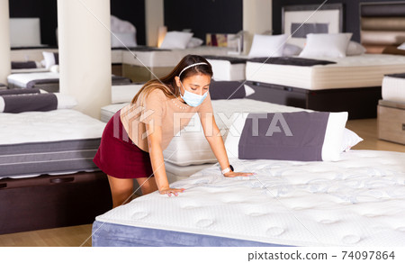 Woman wearing protective mask choosing mattress at store Woman wearing protective mask choosing mattress at store 74097864