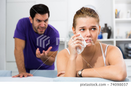 Stressed woman at table with screaming husband behind Stressed woman at table with screaming husband behind 74098037