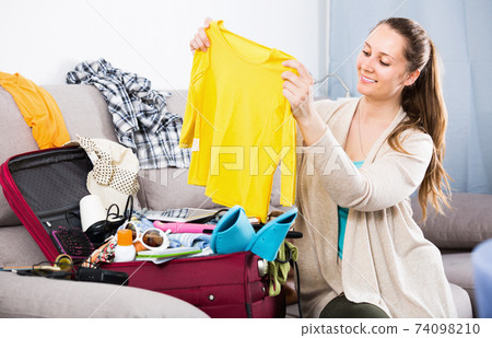 Happy brunette woman packing suitcases at home Happy brunette woman packing suitcases at home 74098210