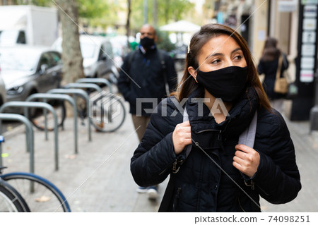 Woman in protective mask on city street with man in background Woman in protective mask on city street with man in background 74098251