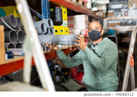 Craftsman in protective mask selects plastic plumbing pipes in hardware store 74098312