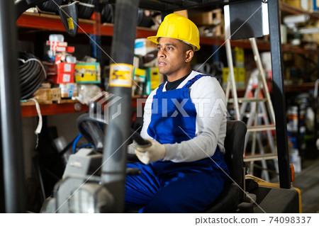 Confident hispanic worker driving forklift in building materials store Confident hispanic worker driving forklift in building materials store 74098337