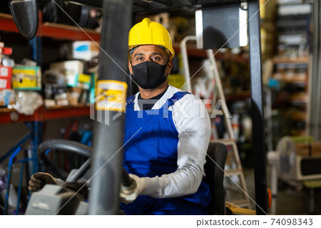 Foreman drives forklift in protective mask at the warehouse of hardware store Foreman drives forklift in protective mask at the warehouse of hardware store 74098343