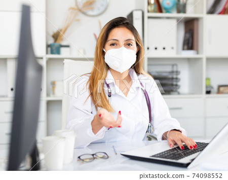 Female doctor in face mask working on laptop 74098552