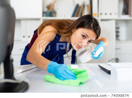 Mexican woman wearing uniform cleaning table in office Mexican woman wearing uniform cleaning table in office 74098674