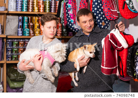 Father and son choose clothes for dogs in pet store Father and son choose clothes for dogs in pet store 74098748