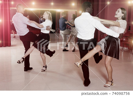 Young positive people dancing vigorous jive movements in dance studio Young positive people dancing vigorous jive movements in dance studio 74098756