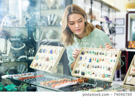 View through showcase glass of woman choosing gemstones jewelry 74098789