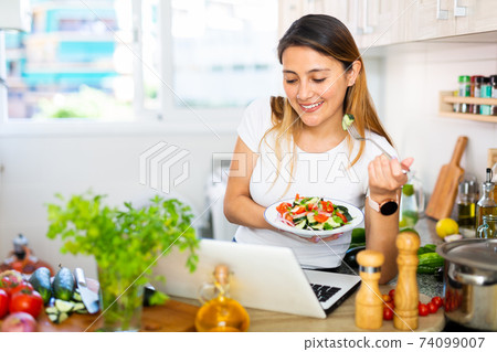 Peruvian housewoman eating salad and watching movie on laptop 74099007