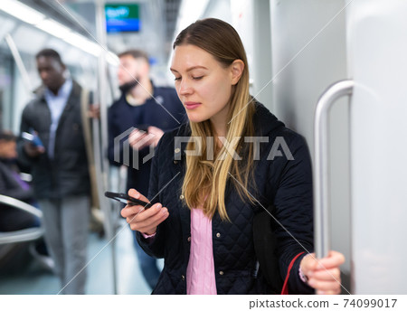 Young woman browsing on phone in metro car Young woman browsing on phone in metro car 74099017