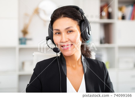 Smiling young female operator talking with customer using headset at office Smiling young female operator talking with customer using headset at office 74099166