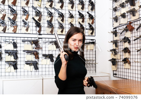 Positive woman with two revolvers in hands in gun shop Positive woman with two revolvers in hands in gun shop 74099376