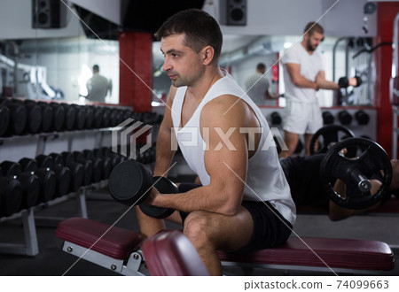 Man exercising with dumbbells in gym Man exercising with dumbbells in gym 74099663