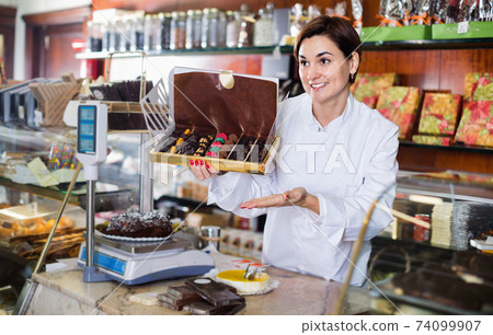 Female seller offering large box of chocolates 74099907