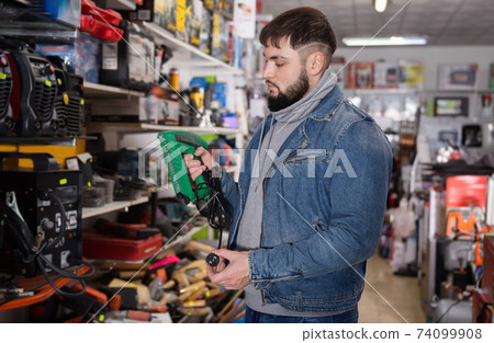 Positive male is standing with new impact wrench in tools store 74099908
