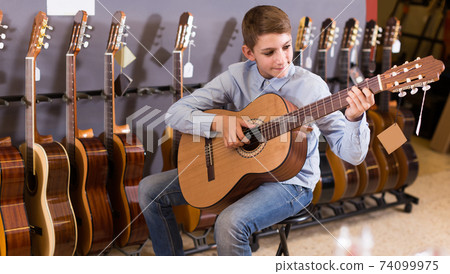 Teenage boy choosing best acoustic guitar in musical shop Teenage boy choosing best acoustic guitar in musical shop 74099975