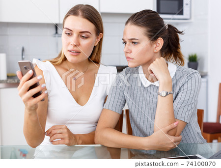 Friends using smartphone in kitchen Friends using smartphone in kitchen 74100070