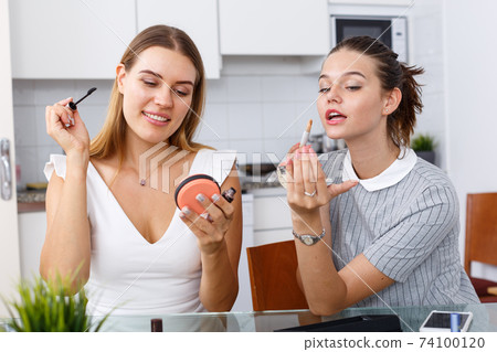 Two positive young female friend doing make up at table with cosmetics 74100120