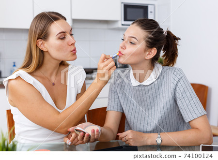 Young female doing make-up for female friend at table with cosmetics 74100124