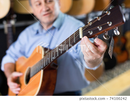 Adult guitarist is playing on acoustic guitar in music store. Adult guitarist is playing on acoustic guitar in music store. 74100242