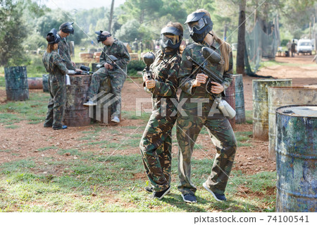 Cheerful young women friends in camouflage holding guns ready for playing paintball Cheerful young women friends in camouflage holding guns ready for playing paintball 74100541