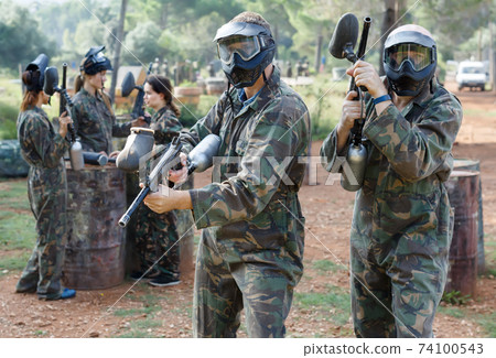 Two vigorous paintball players in full gear having fun outdoors Two vigorous paintball players in full gear having fun outdoors 74100543