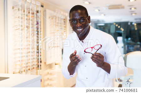 Male optician standing and offering glasses in shop Male optician standing and offering glasses in shop 74100681