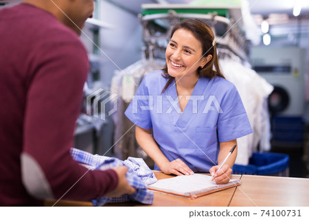 Friendly laundry worker talking to customers at reception 74100731