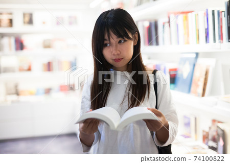 Young female student choosing new books on shelves Young female student choosing new books on shelves 74100822