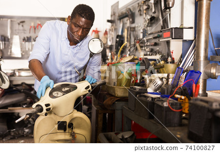 Confident man worker repairing motorcycle in workshop Confident man worker repairing motorcycle in workshop 74100827
