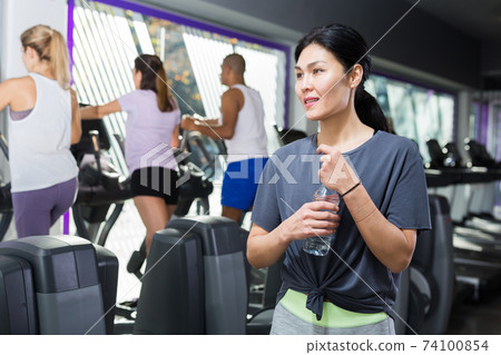 Woman standing with drinking water in gym 74100854