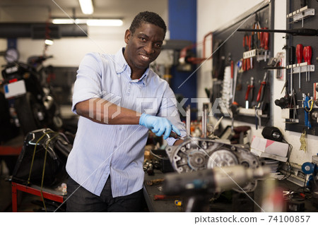 Afro american worker repairing a motorcycle engine in a garage 74100857
